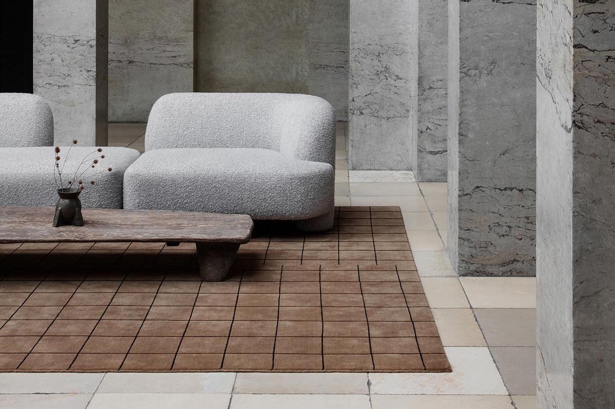 Minimalist sitting area with curved grey sofa, low wooden table and geometric brown rug from Nordic Knots' new Grid collection | New finds - November 2021 | These Four Walls blog