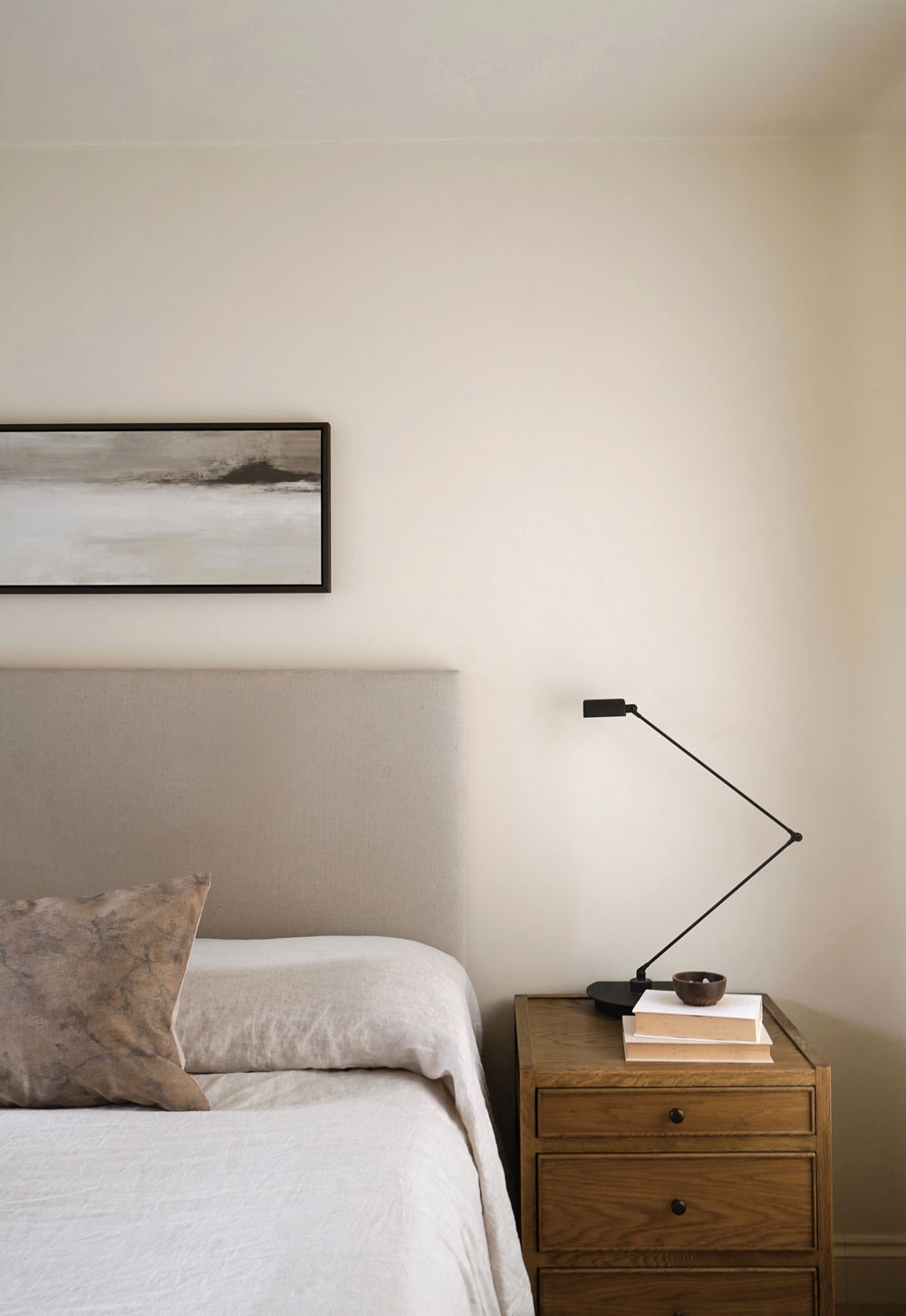 Rustic-minimalist cottage bedroom in calming beige, with linen curtains, oak bedside table, linen bedding, tapestry cushion and neutral abstract landscape painting | Art for awkward spaces with Atelier Printworks | These Four Walls blog