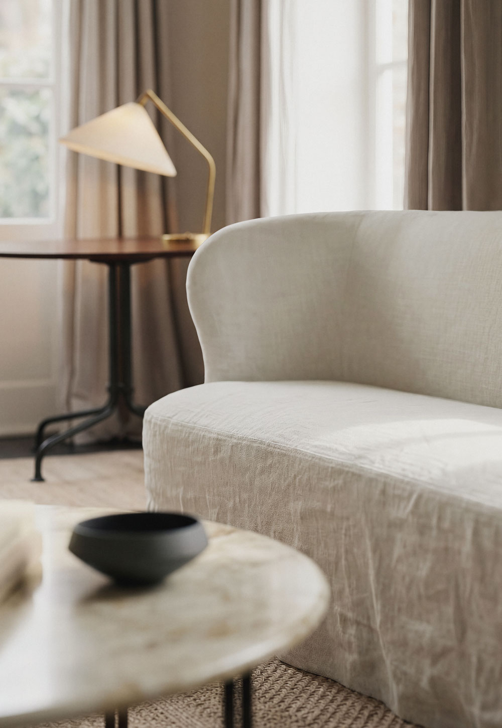 Calm neutral living room with dark wood furniture, natural materials and beige linen slipcover sofa from GUBI's 'Stay' collection | New design finds - July 2026 | These Four Walls blog