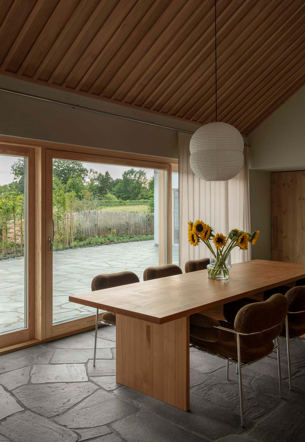 Warm, minimalist kitchen-diner with exposed timber ceiling, flagstone floor, lig sheer beige curtains and bespoke wooden dining table | Home tour - a contemporary take on a traditional Swedish longhouse in Österlen, Skåne | These Four Walls blog