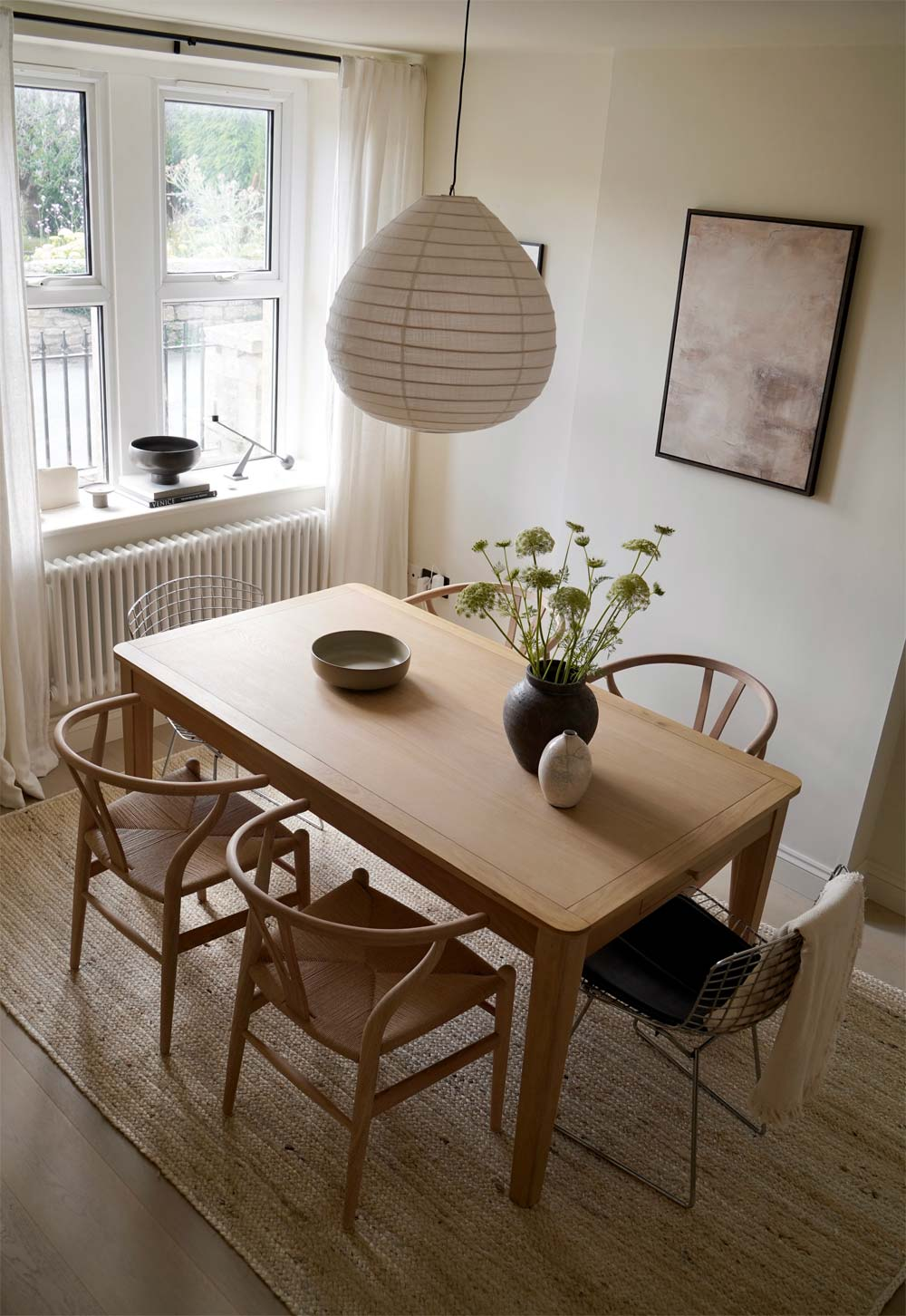 Pale oak table, Wishbone chairs, neutral decor, linen curtains and pendant light, jute rug and gallery wall in a rustic-minimalist cottage dining room | These Four Walls blog