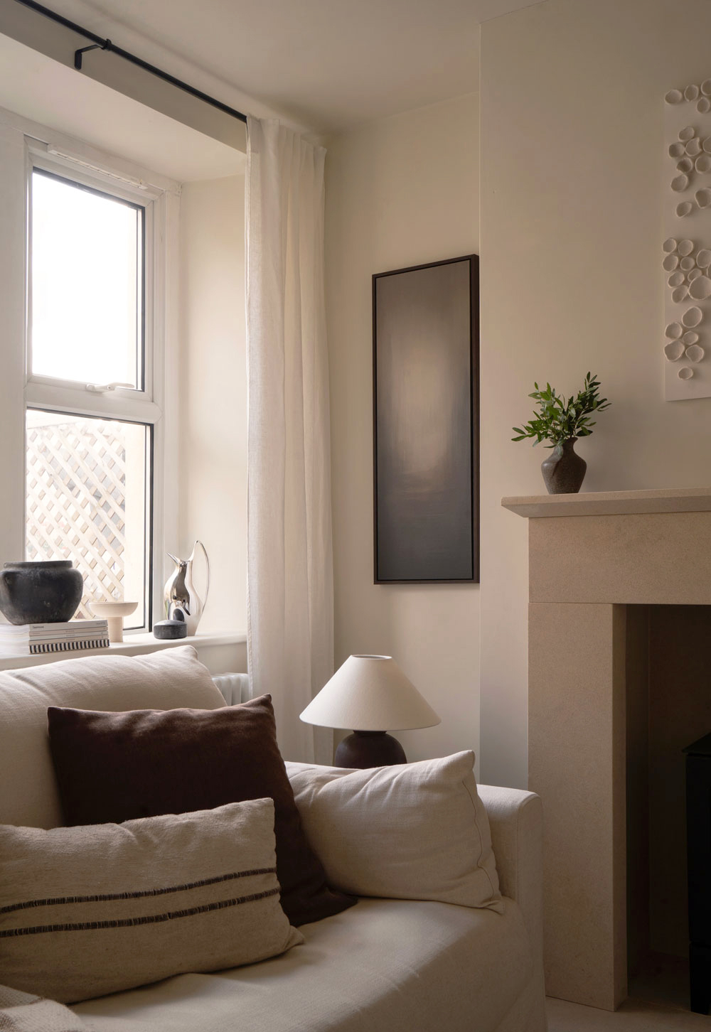 Linen slipcover sofa, stone fireplace, abstract art and stoneware-based table lamp in a minimalist cottage interior | These Four Walls blog