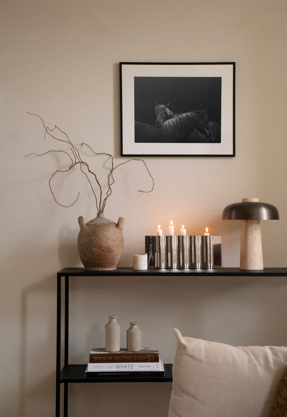Minimalist black console table with vintage urn, foraged branches, stainless-steel candleholder and bronze and travertine table lamp | These Four Walls blog
