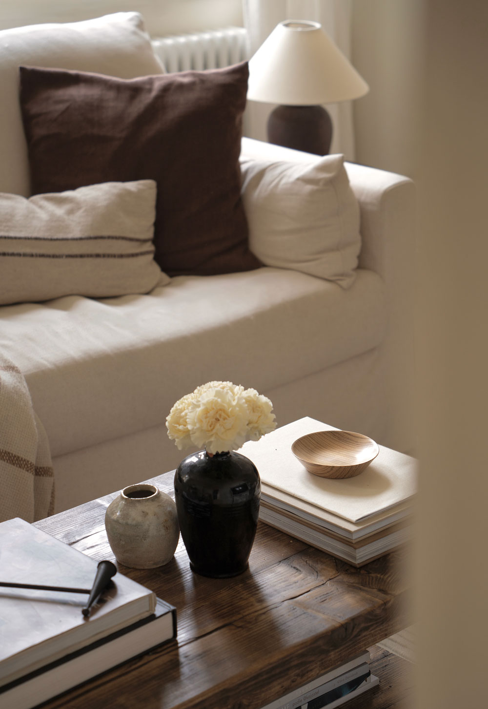 Rustic wooden coffee table, beige linen slipcover sofa and vintage vases in a minimalist cottage living room | These Four Walls blog